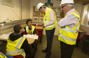 Four construction workers in safety vests and helmets discussing HR documents inside a site office. Four construction workers in safety vests and helmets discussing HR documents inside a site office.